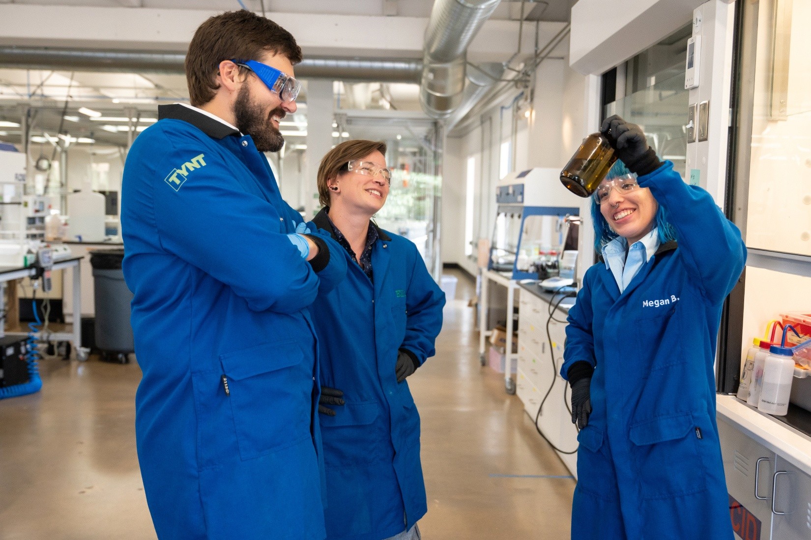 Three people in blue lab coats stand in a science lab