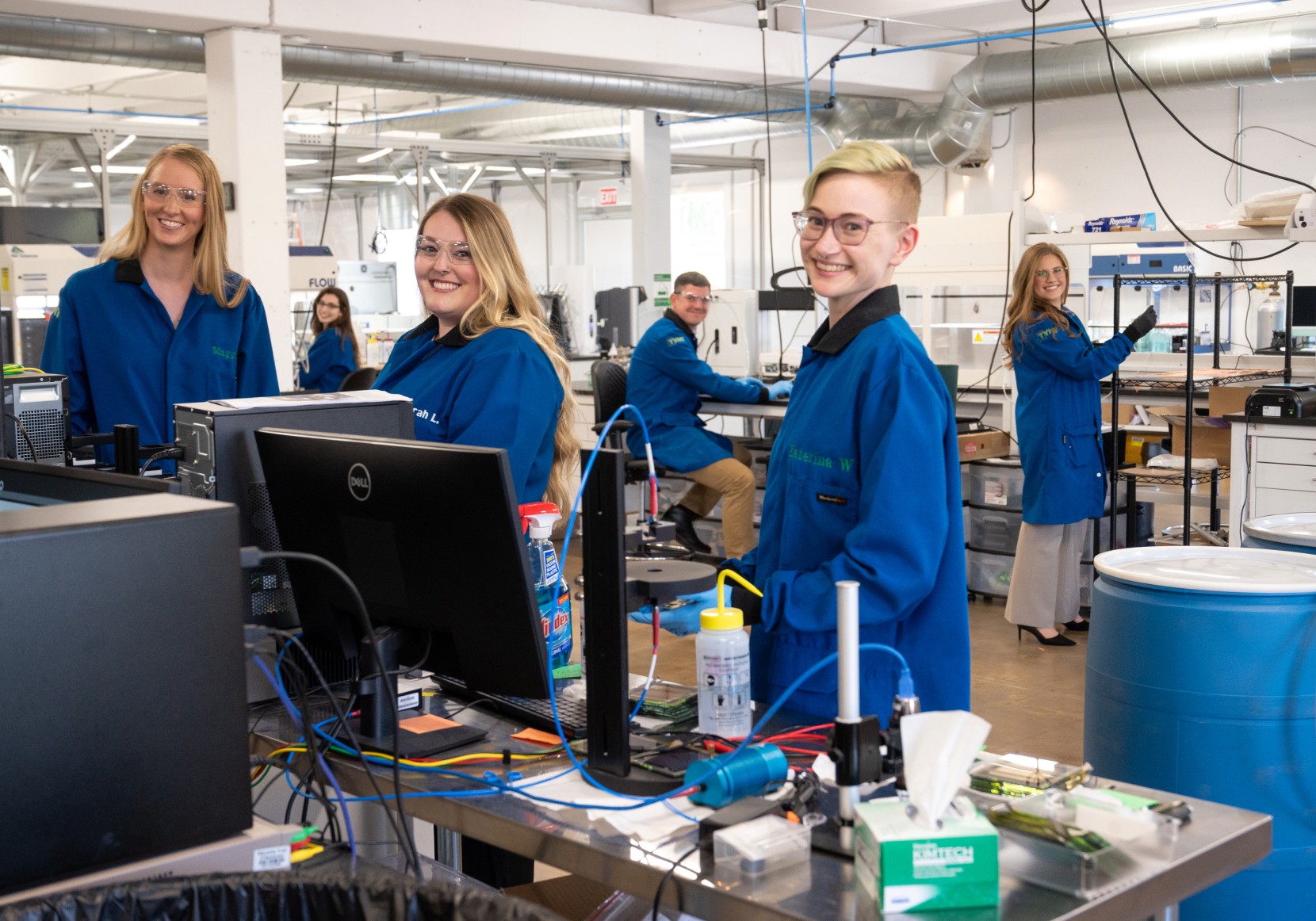 Several people in blue lab coats are working in a science lab.